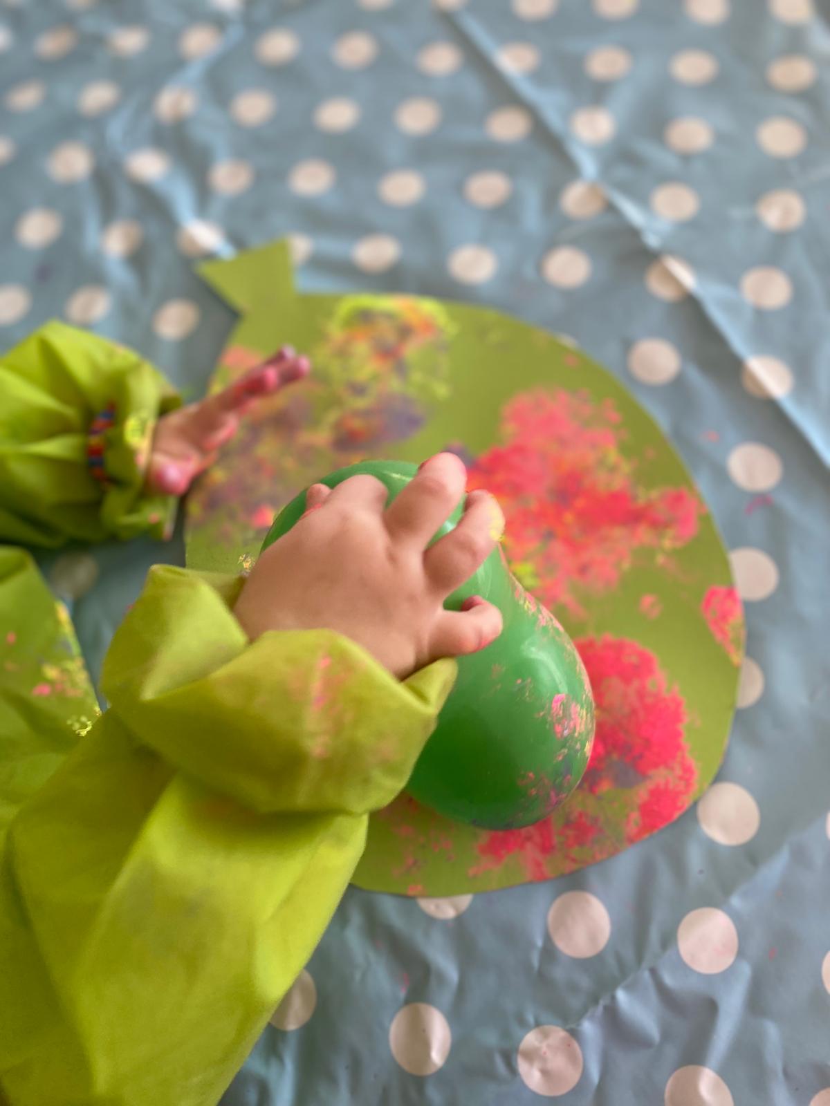 Kinderhände drucken mit einem Luftballon rosa Farbe auf grünes Papier