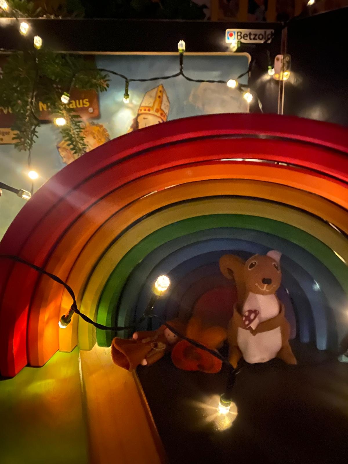 Bunter Holzregenbogen mit Lichterkette, in der Mitte ein kleiner Stoffbär