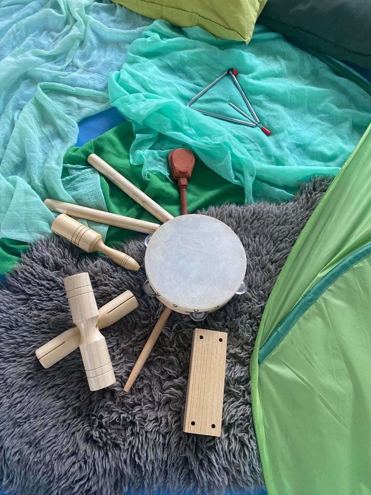 Holzinstrumente, Triangel und Handtrommel auf einem grauen Fell und mintgrünen Tüchern