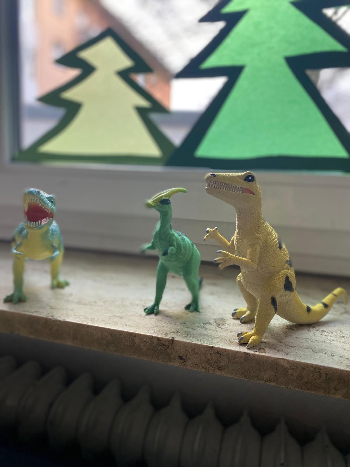 Spielzeug-Dinosaurier auf der Fensterbank, dahinter Tannen aus Transparentpapier