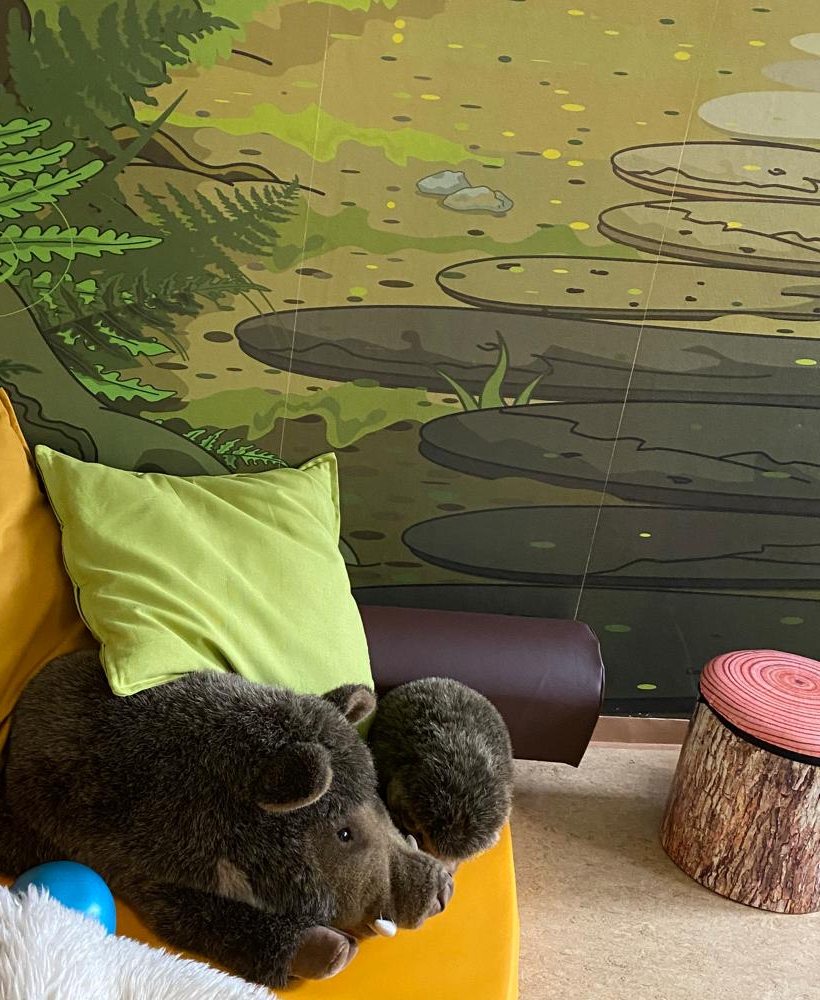Kuschelecke mit Kissen, einem Wildschwein-Plüschtier und einem Waldmotiv an der Wand
