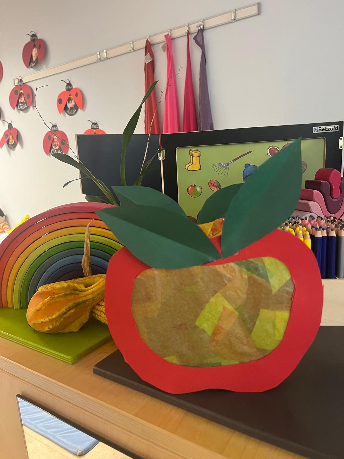 Selbstgebastelter Apfel aus Transparentpapier vor einem Holzregenbogen